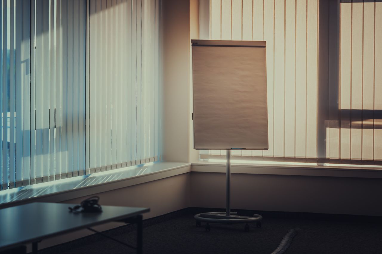 Crafting Captivating Headlines: Your awesome post title goes here A quiet, empty meeting room featuring vertical blinds, flipchart stand, and soft lighting, perfect for business presentations.