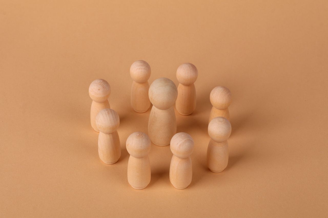 Wooden peg dolls arranged in a circle on a soft brown background. Minimalist concept of community or teamwork.